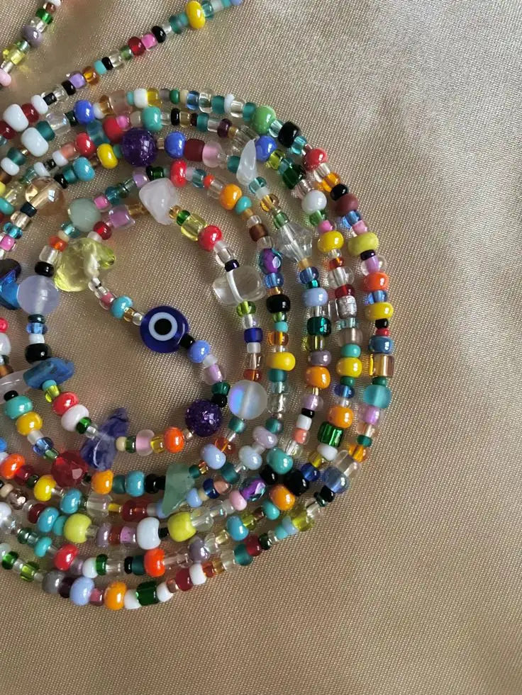 Un collier vibrant à multiples rangs, fait de perles, avec un mélange de perles de verre et de cristal colorées, agrémenté d’un pendentif en forme d’œil.